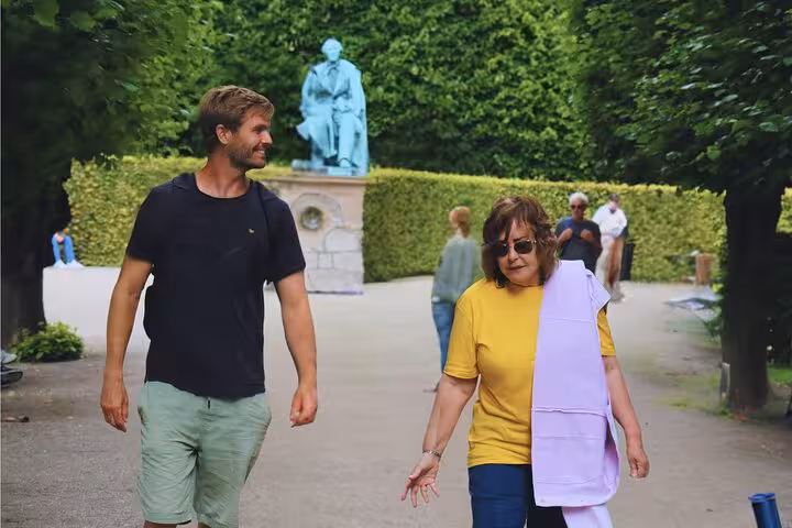 Tourists enjoying a leisurely walk in a scenic park in Old Copenhagen with a historic statue in the background.