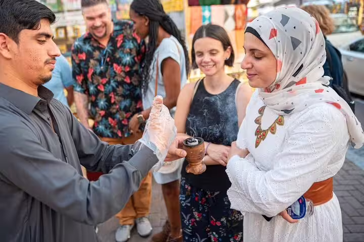 Small group on a guided walking tour in Old Dubai tasting traditional snacks from a local street vendor in the souk