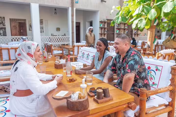Visitors share Emirati snacks and stories with a local guide at a traditional courtyard café on a Dubai walking food tour