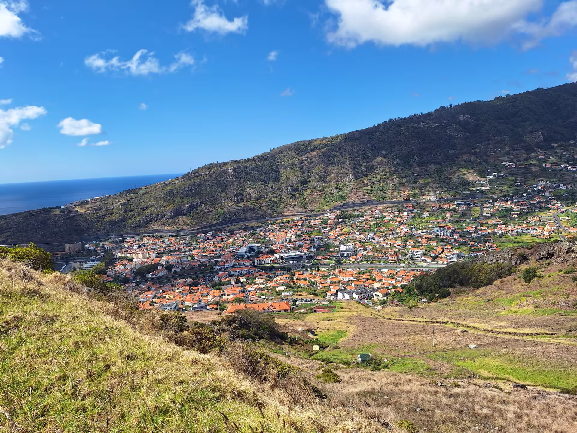 Vibrant coastal town view from The Old Path's Hike, showcasing red-tiled rooftops and lush hills under a clear blue sky.
