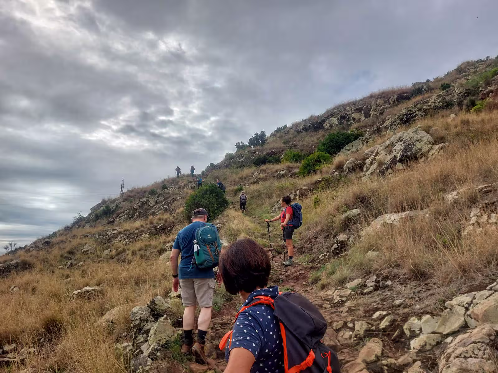Group of hikers trekking uphill on a rugged path under a cloudy sky on The Old Path's Hike tour.