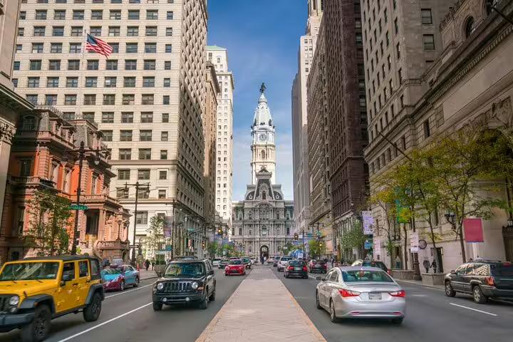 Busy street view of Philadelphia City Hall tower along a traffic-filled urban boulevard with historic buildings