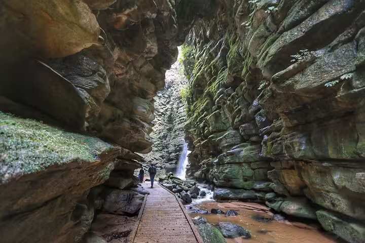 Walk through the dramatic canyon passage leading to a hidden waterfall at Old Town State Park, surrounded by towering cliffs.