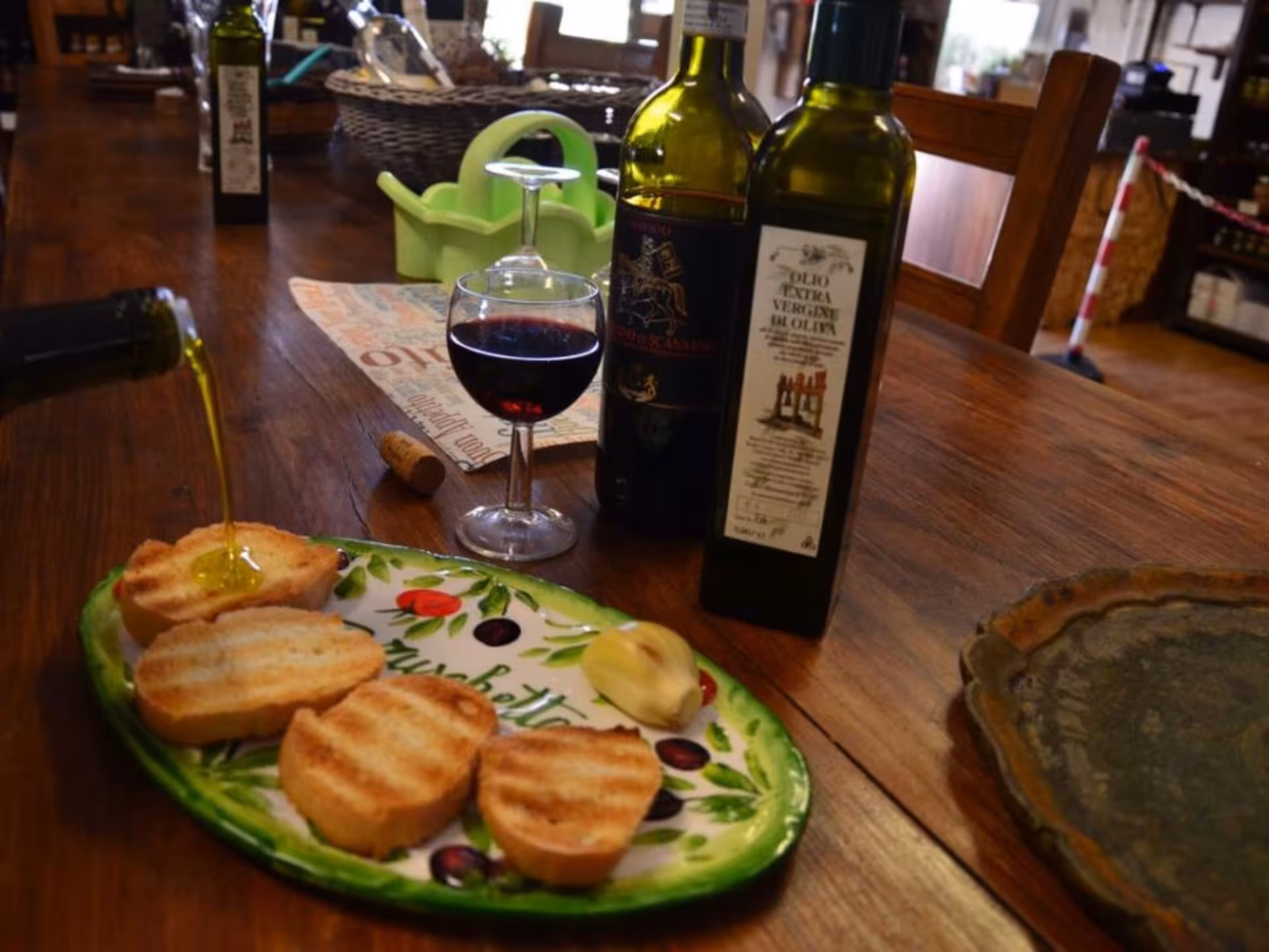 Olive oil being poured over toasted bread with wine bottles and a glass on a wooden table during Chianciano tasting tour.