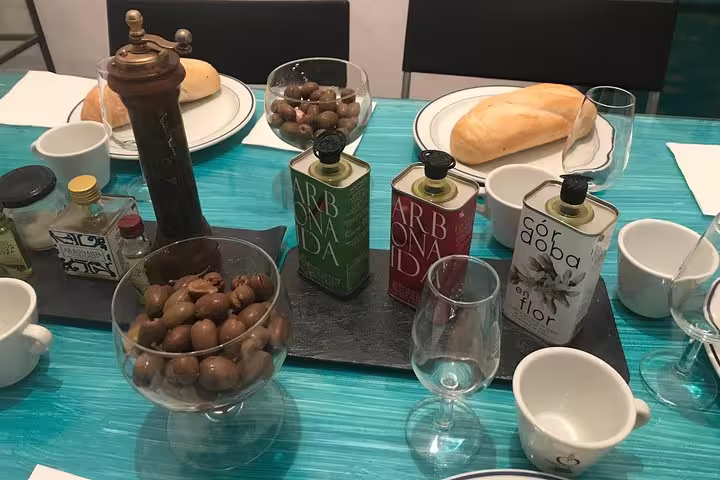Close-up of olive oil tasting setup in Cordoba featuring artisanal oils, fresh bread, and olives on a vibrant table.