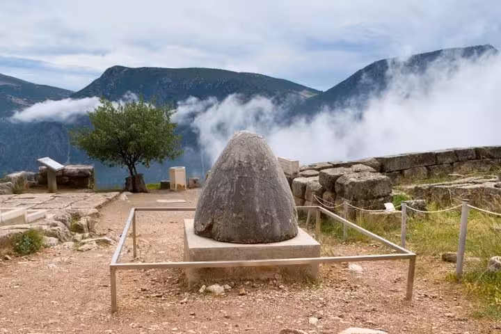 Omphalos stone at ancient Delphi sanctuary with misty mountains, featured on a luxury Delphi day tour