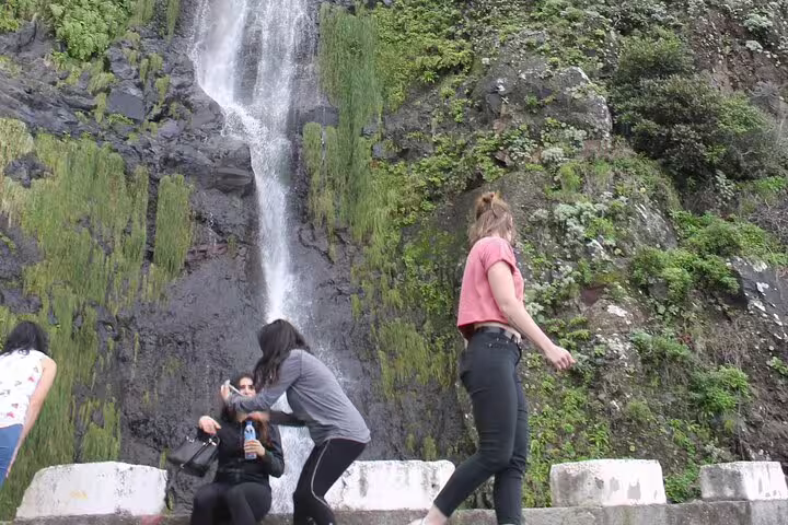 Tourists enjoy a scenic waterfall stop during the Full Day Open Roof 4x4 adventure in the lush northwest of Madeira.