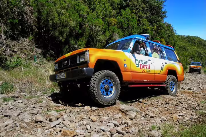 Orange 4x4 vehicle navigating rugged terrain on a sunny day during a full-day private adventure tour in Madeira's scenic landscape.