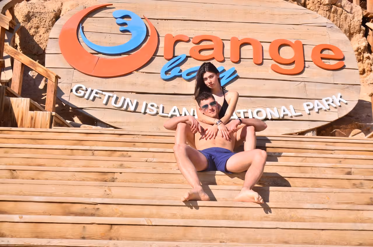 Couple relaxing by the Orange Bay Giftun Island sign, a popular stop on Hurghada snorkeling trip with lunch