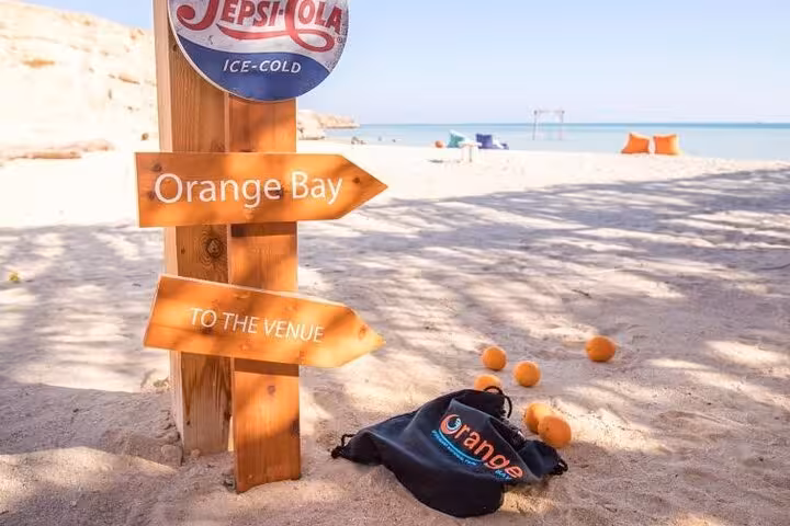 Orange Bay sign on sandy beach with oranges and sea view, meeting point for Hurghada island tour with drinks