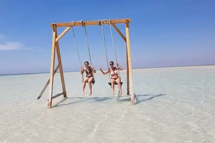Travelers on wooden sea swing in crystal-clear water at Orange Bay Island, Hurghada VIP snorkeling boat tour