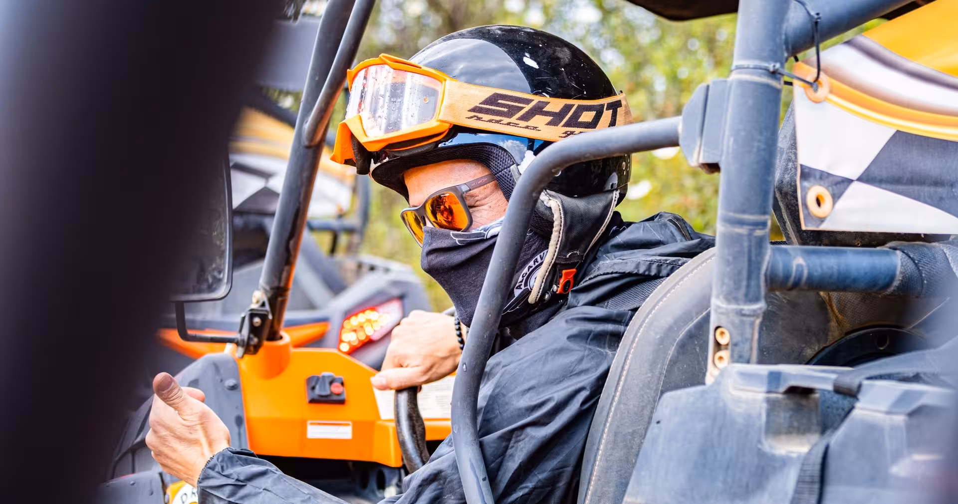 Close-up of a helmeted driver gripping the wheel of an orange buggy, ready for a thrilling Algarve off-road adventure tour