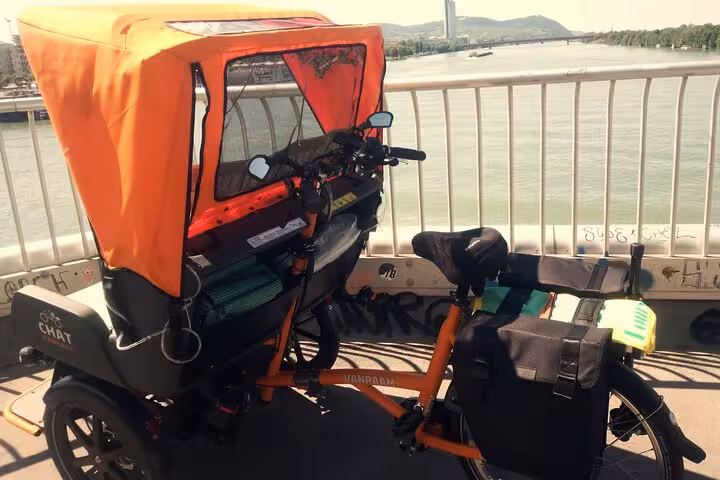 Orange e-rickshaw on Danube bridge, scenic stop on big private Vienna tour by RAXI e-rickshaw