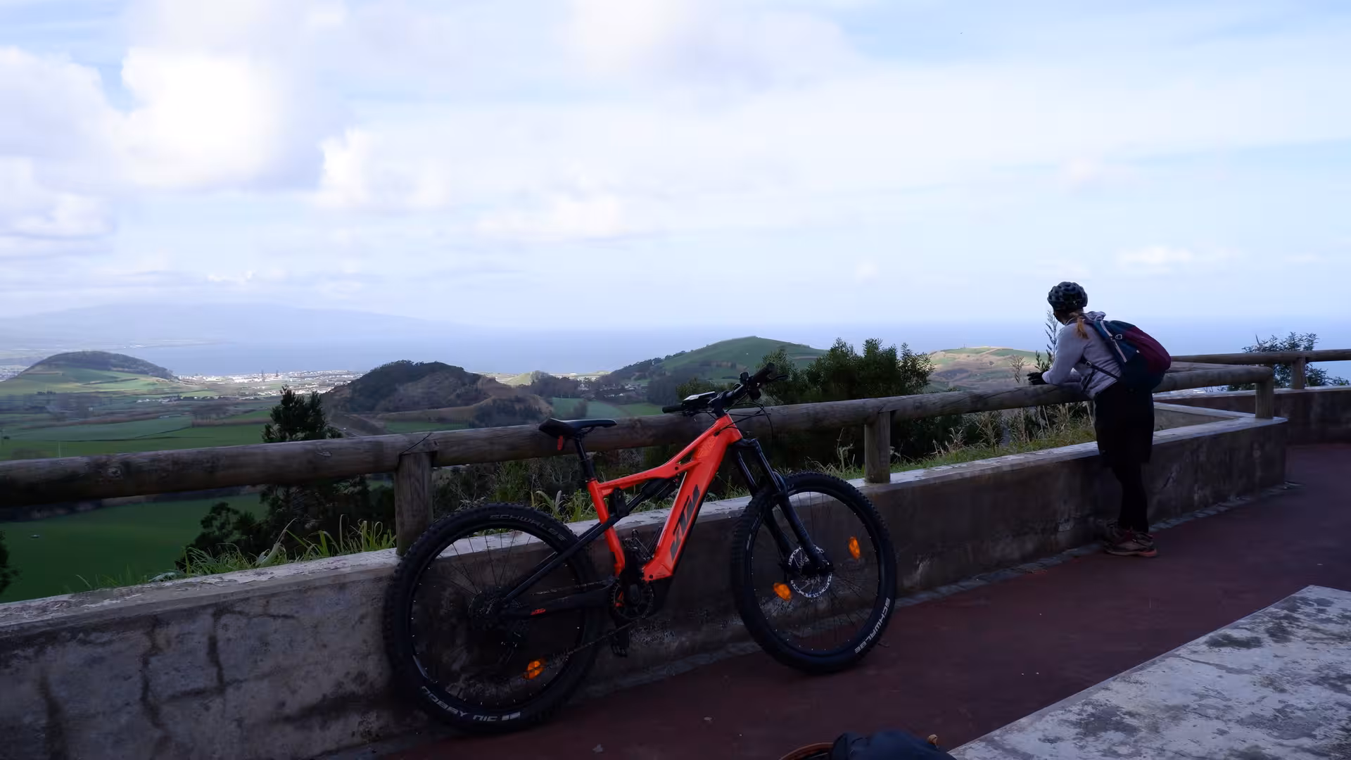 Bright orange e-bike parked at a Ribeira Grande viewpoint as a cyclist enjoys sweeping ocean and volcanic landscape views