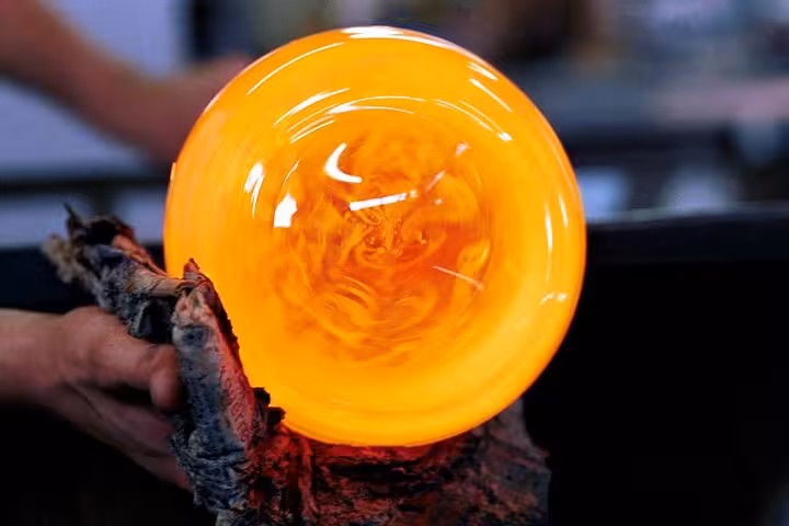 Close-up of a vibrant orange glass sphere being crafted by a skilled glassblower on a private art tour.