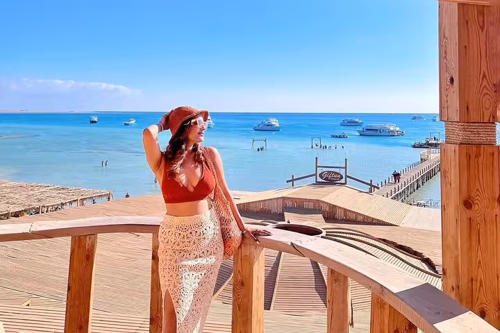 Traveler on wooden pier overlooking Orange Island lagoon in Hurghada, Red Sea boats on snorkeling trip with lunch