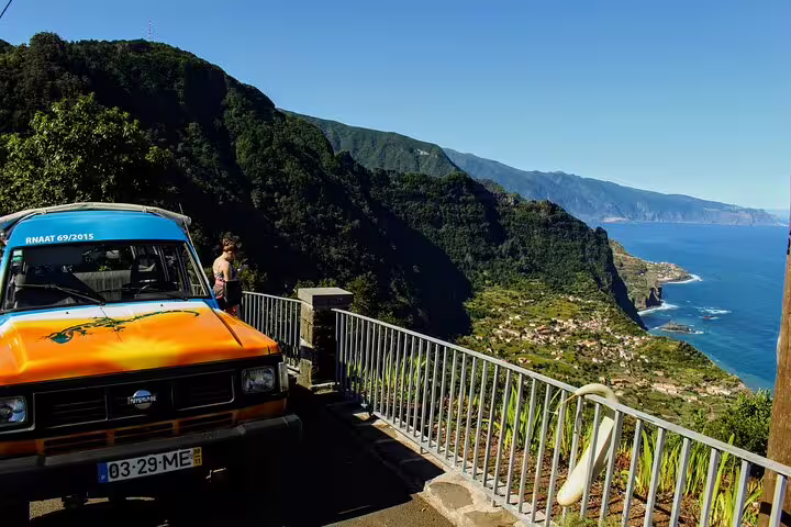 Vintage orange jeep on a scenic overlook in Northeast Madeira with lush green mountains and ocean views on a sunny day.