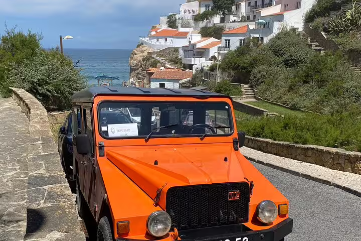 Bright orange jeep parked by the scenic coastal village of Sintra-Cascais with ocean views and charming white houses.