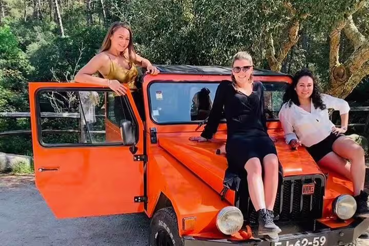Group enjoying a vibrant orange jeep tour through the scenic landscapes of Sintra-Cascais Natural Park.