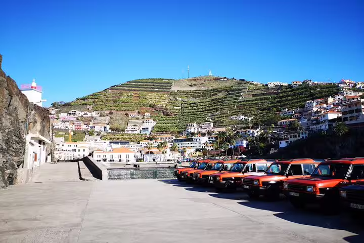 Row of orange jeeps lined up against the picturesque hillside vineyards of Câmara de Lobos, Madeira.