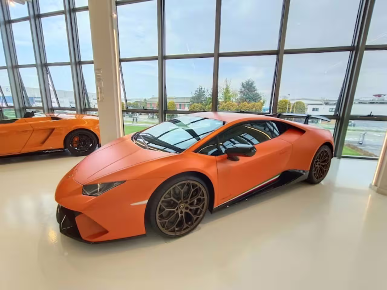 Sleek orange Lamborghini sports car displayed in Museo Lamborghini with large windows and modern design.