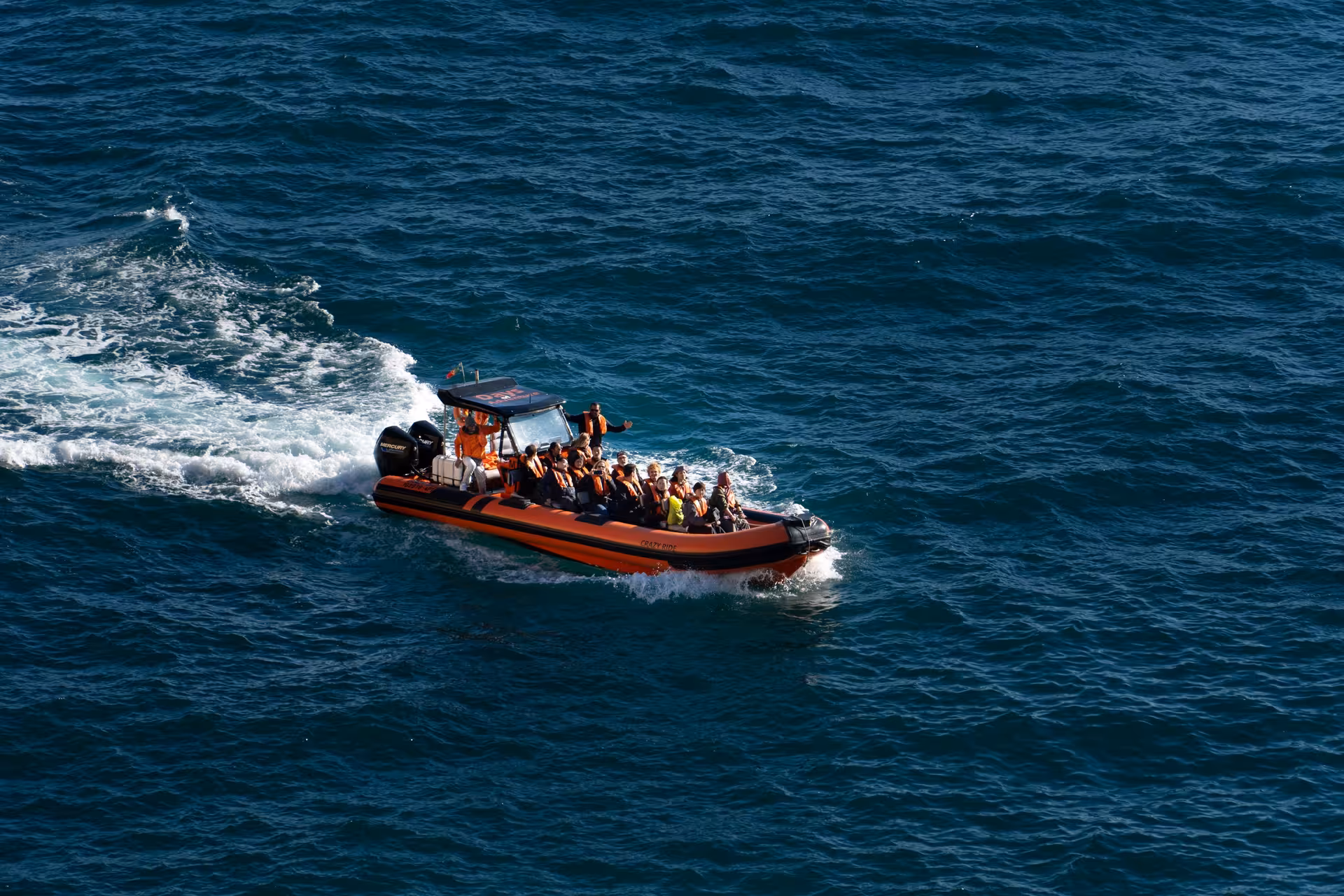Orange speed boat filled with tourists wearing life jackets speeding across deep blue Atlantic Ocean on Benagil cave tour