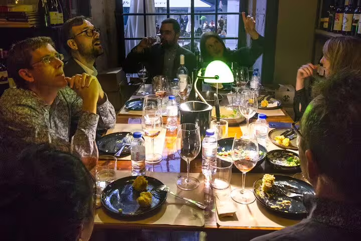 A group of people enjoying an intimate natural and organic wine tasting and food pairing experience around a warmly lit table.