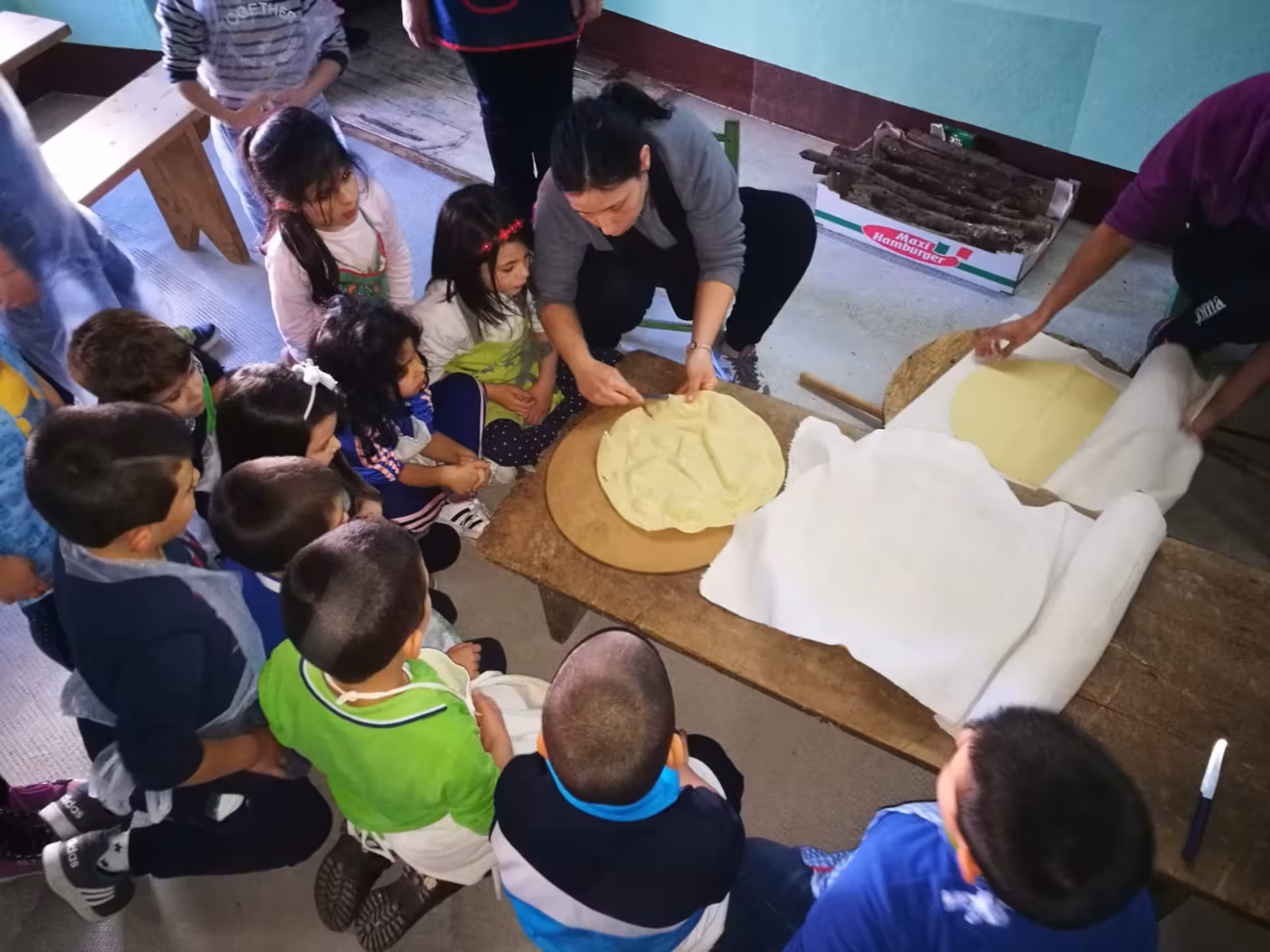 Children attentively watch as a guide demonstrates traditional carasau bread-making techniques in Orgosolo.
