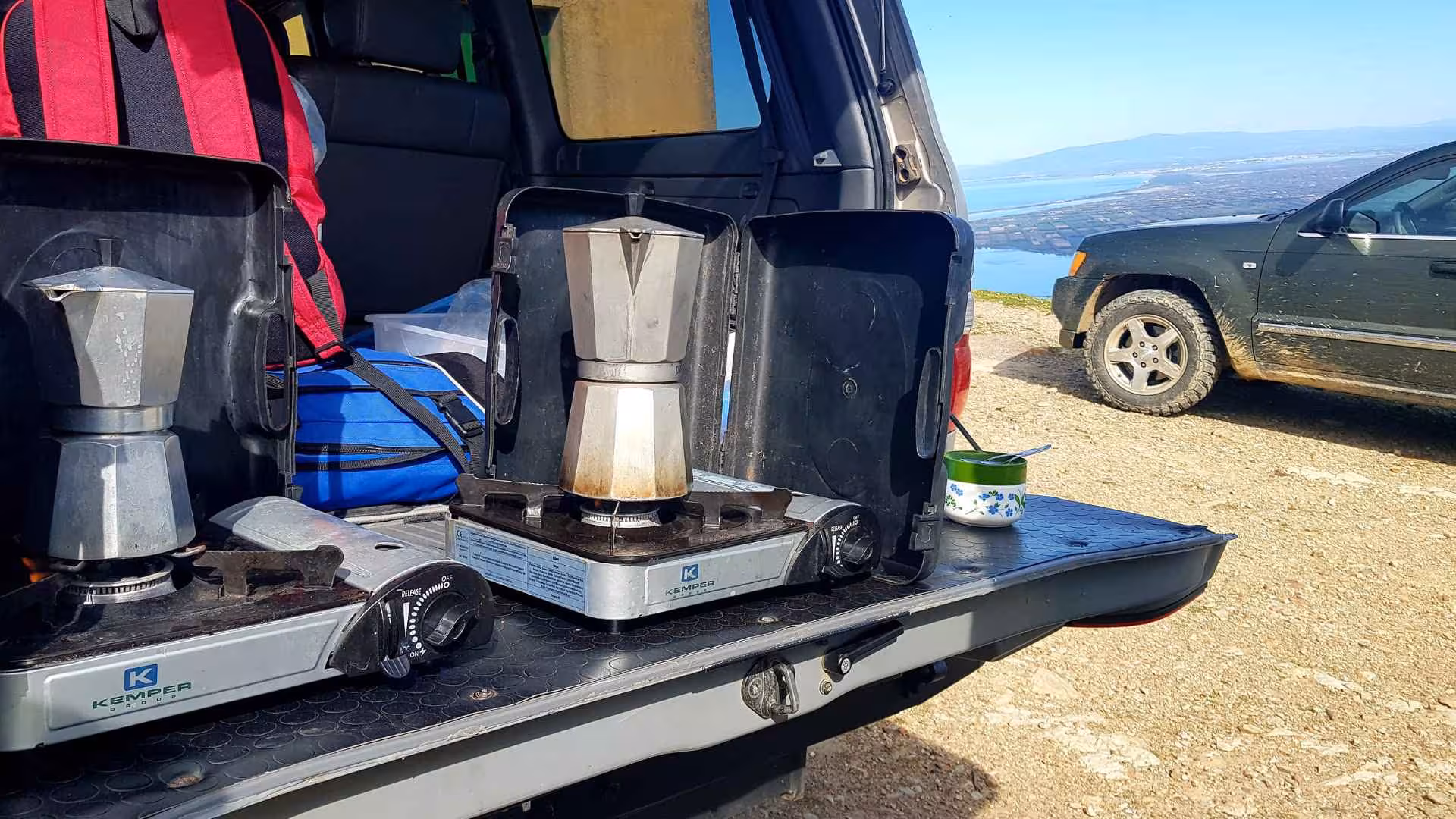 Off-road adventure with coffee setup on SUV tailgate overlooking scenic Costa Verde landscape.