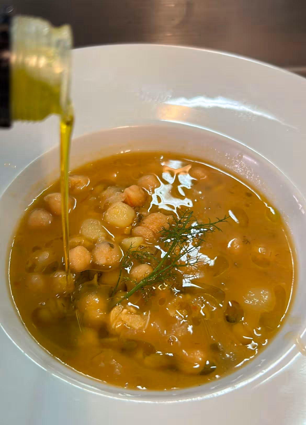Fresh olive oil being poured into a bowl of hearty chickpea soup at an Oristano farm tour with oil tasting.