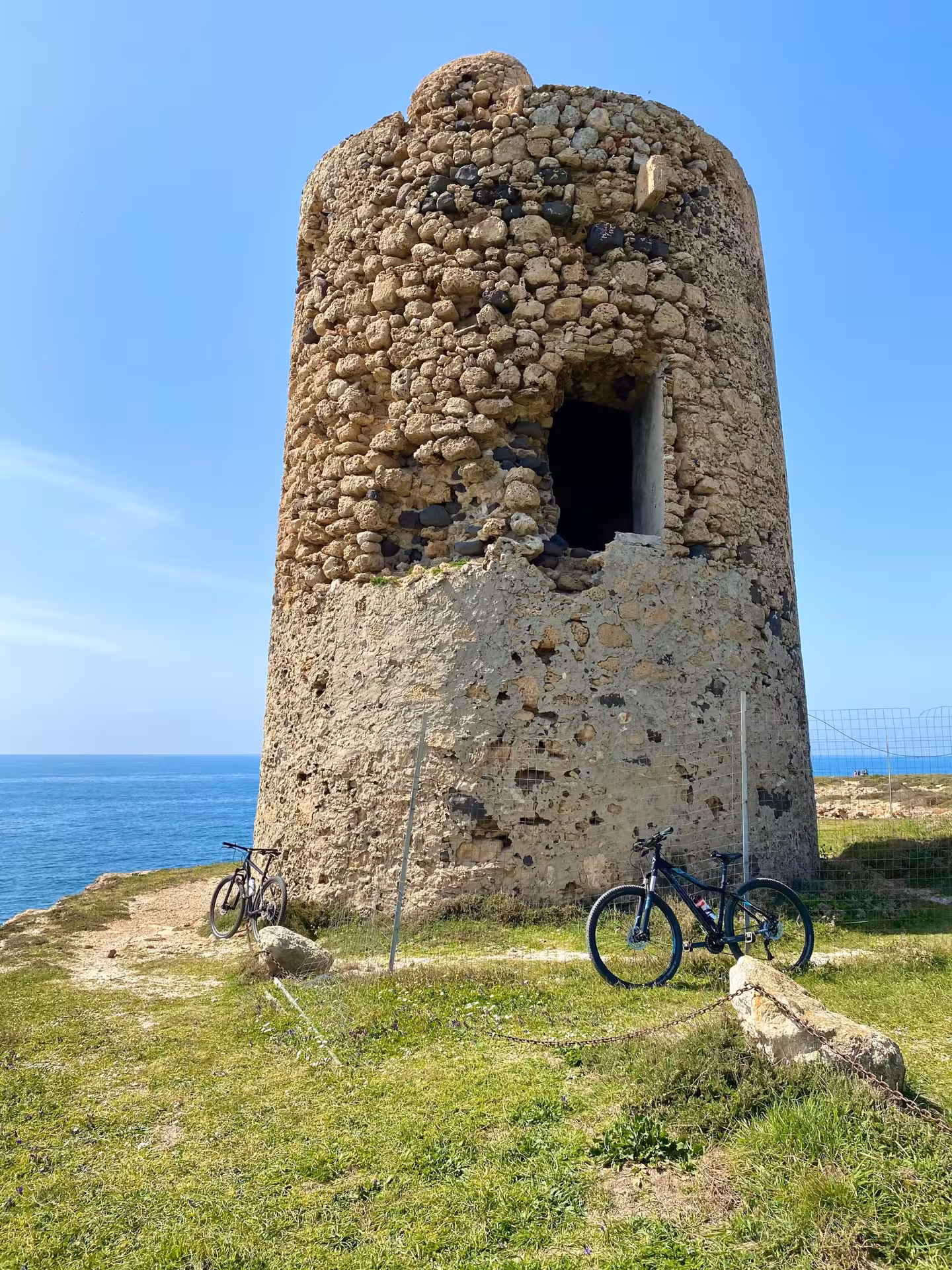 Stone watchtower with bikes on a scenic Sinis Peninsula bike tour from Oristano, overlooking the Mediterranean Sea.