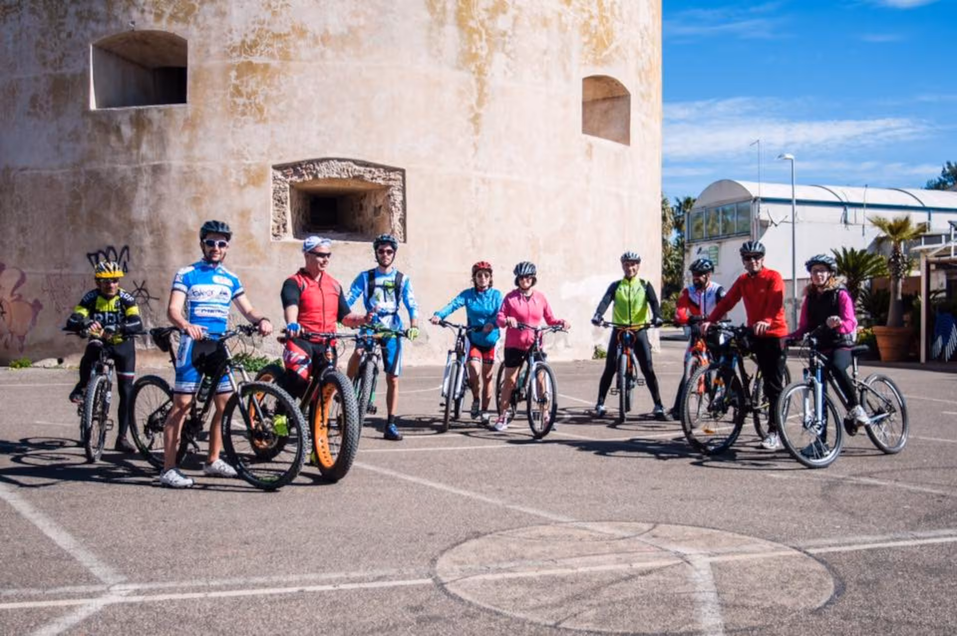 Group of cyclists with bikes at the marina during Oristano's Torregrande coast bike tour under clear skies.