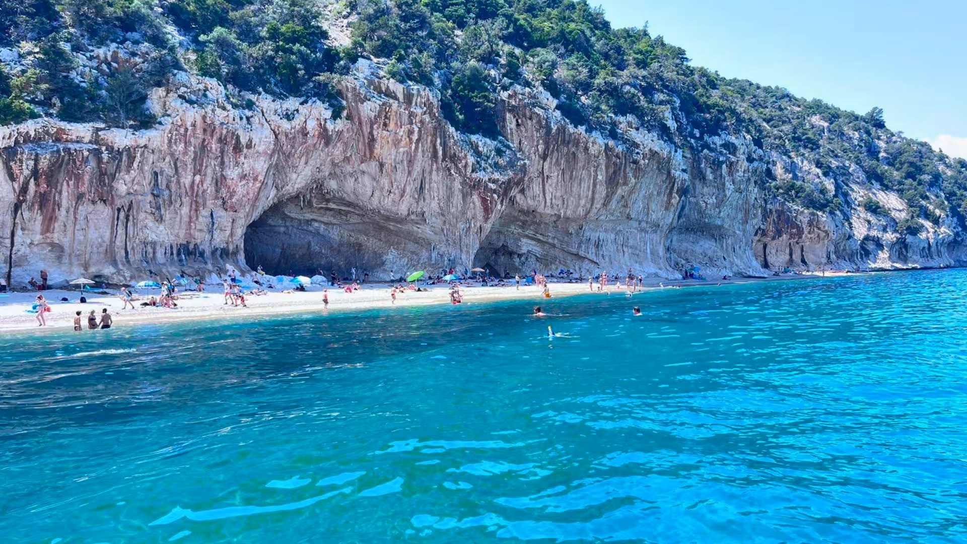 Scenic view of Cala Ginepro's rugged cliffs and turquoise waters on a sunny day in Orosei, Sardinia.