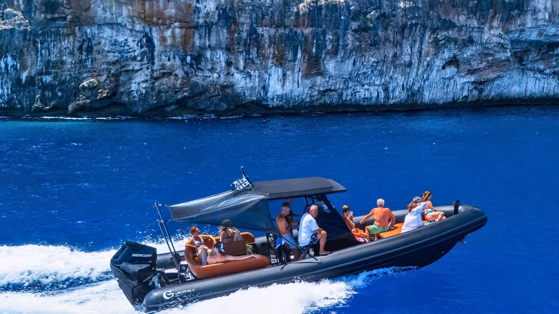 A dinghy speeds through the deep blue sea along the rocky coast between Cala Goloritzè and Cala Luna.