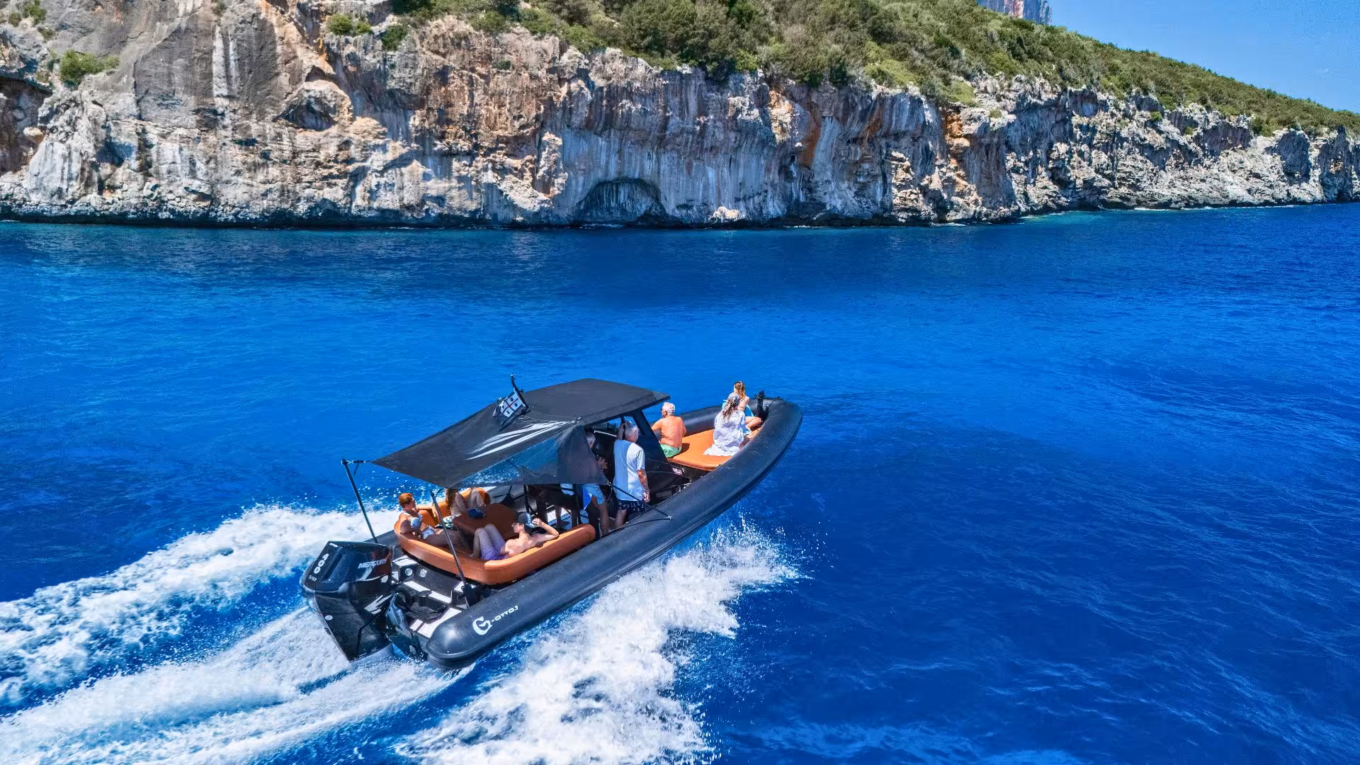 Tourists enjoy a scenic dinghy ride along the stunning cliffs of Cala Goloritzè in crystal-clear blue waters.