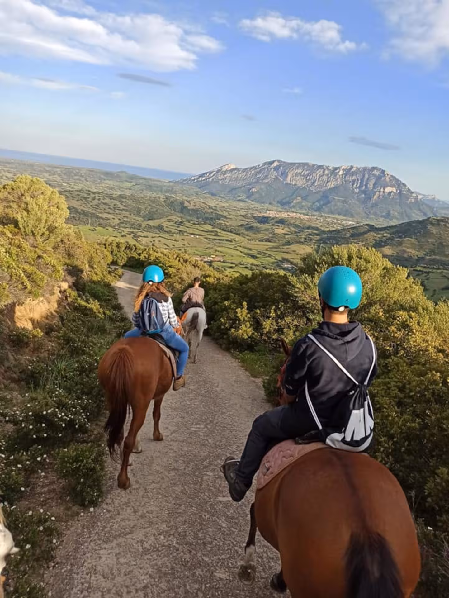 Riders on horses enjoying breathtaking Orosei landscape with mountains under a clear sunrise sky.