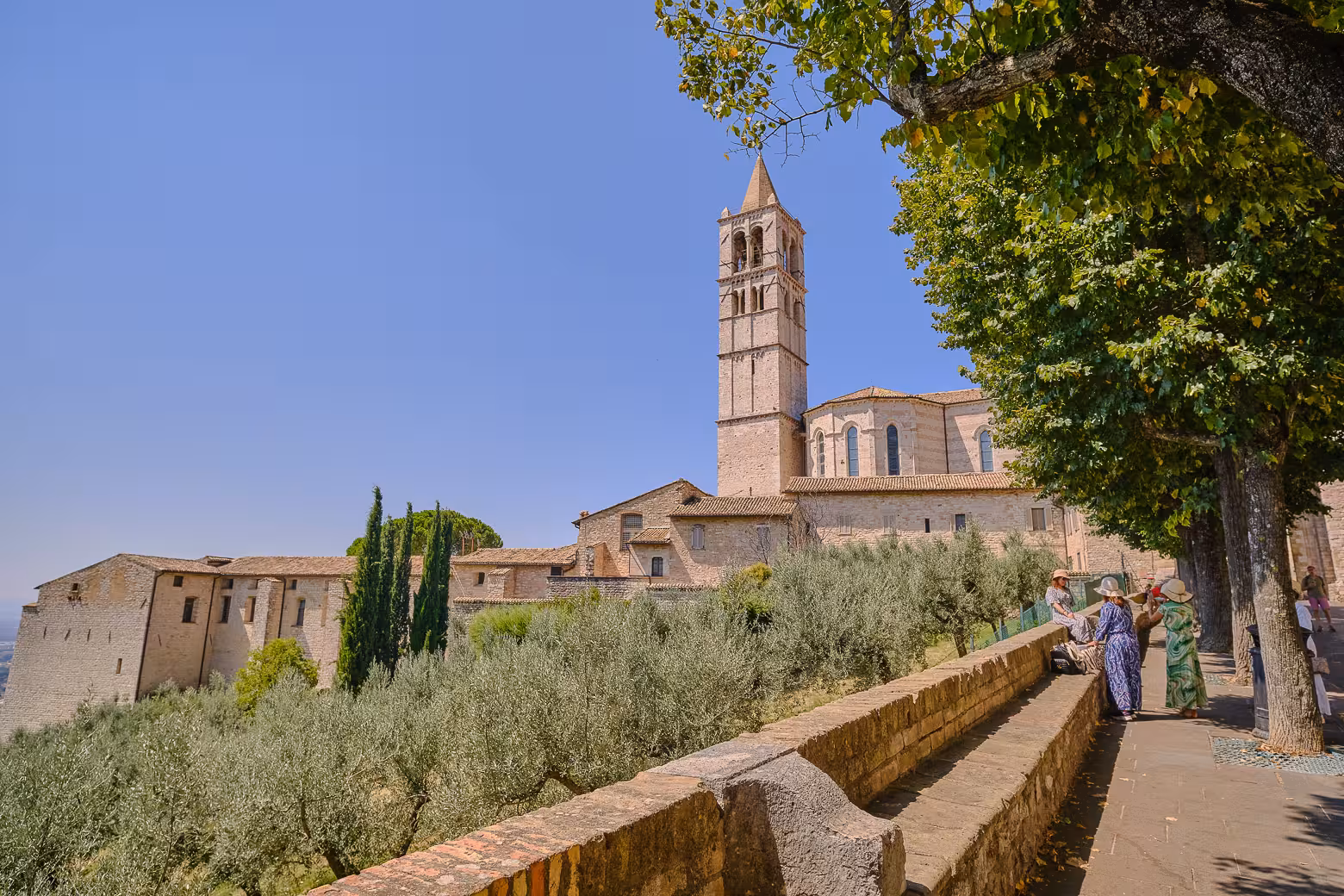 Scenic view of Orvieto's historic bell tower surrounded by lush greenery and tourists enjoying the landscape.