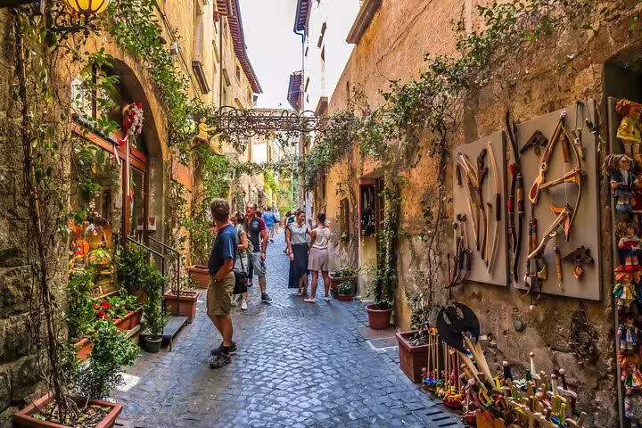 Tourists explore a charming cobblestone street in Orvieto, Italy, lined with quaint shops, during a guided tour from Rome.