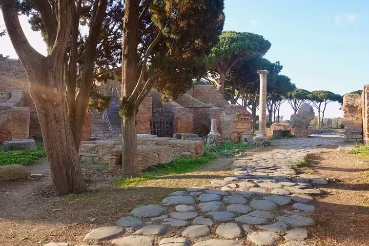 Ancient cobblestone street lined with trees and ruins in Ostia Antica, perfect for a half-day private tour.