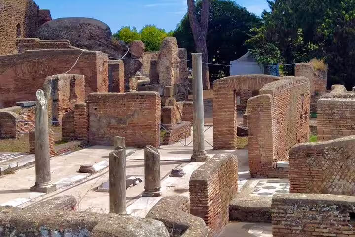 Sunlit brick ruins and marble columns of Ostia Antica archaeological site visited on exclusive boat and walking tour from Rome