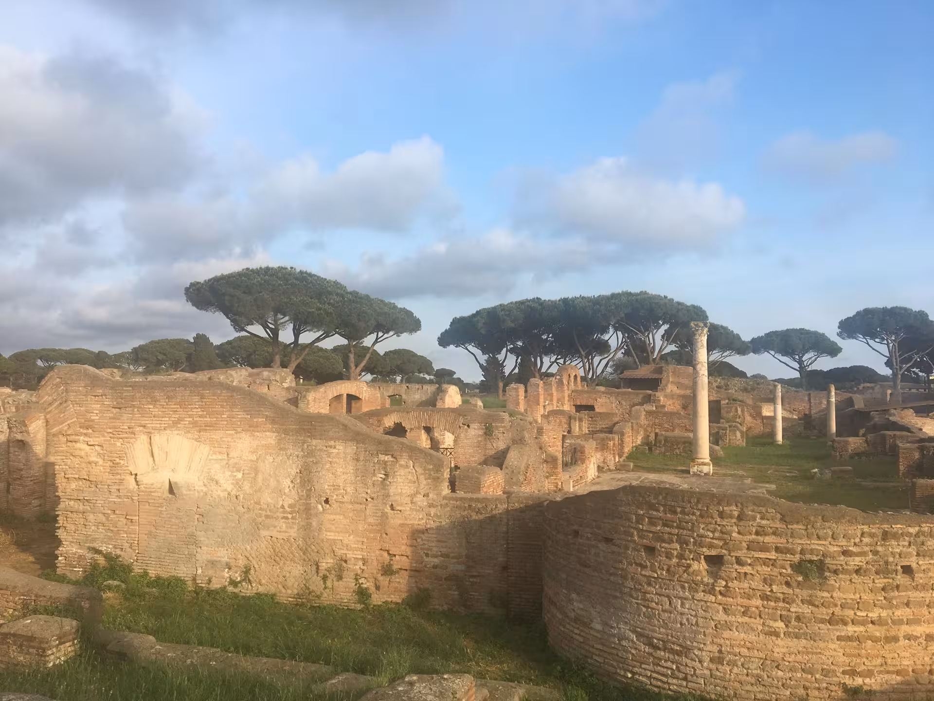 Expansive landscape of Ostia Antica ruins under a clear sky, featuring ancient brick structures and columns.