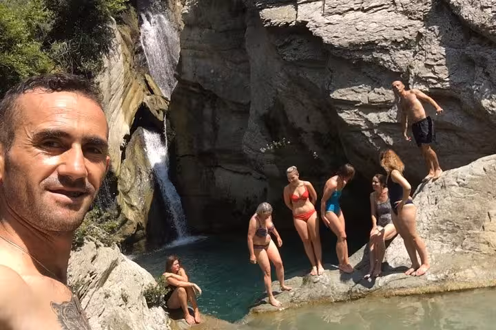 A group of people enjoy the stunning natural pool below Bogove Waterfall, basking in the sunlight and scenery.