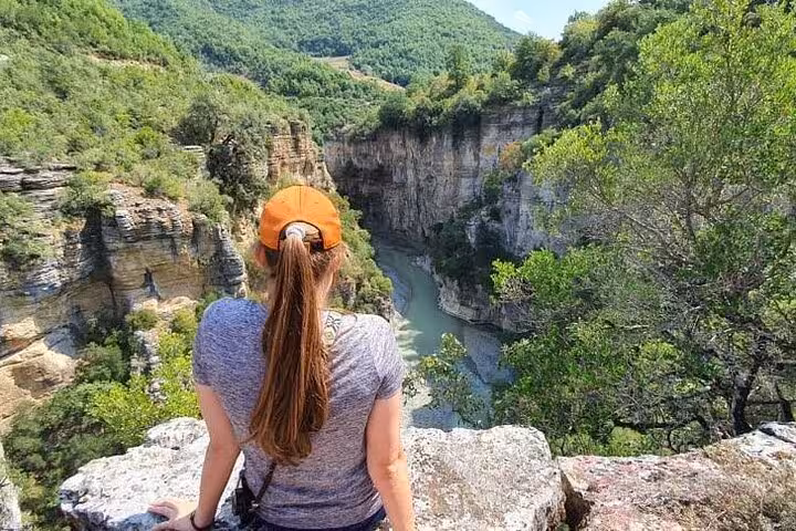 Traveler enjoying a panoramic view of Osum Canyon's lush landscape and winding river from a scenic lookout point.