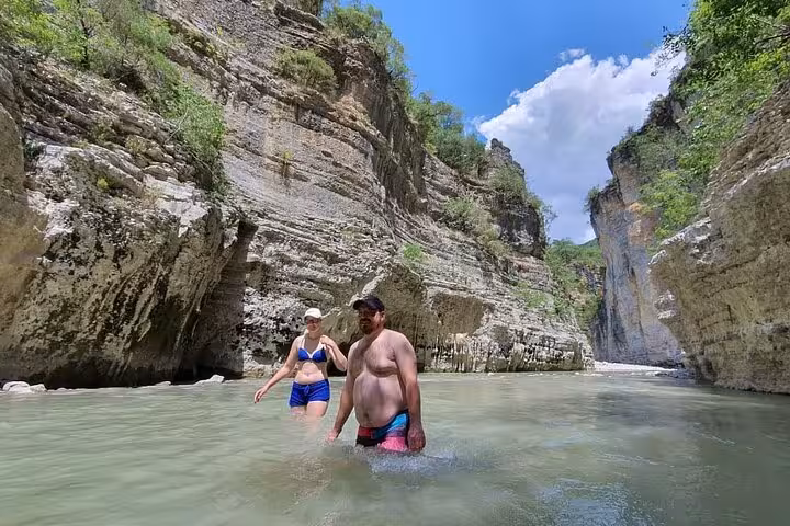 Visitors wading through the refreshing waters of Osum Canyon, surrounded by towering cliffs and vibrant greenery.