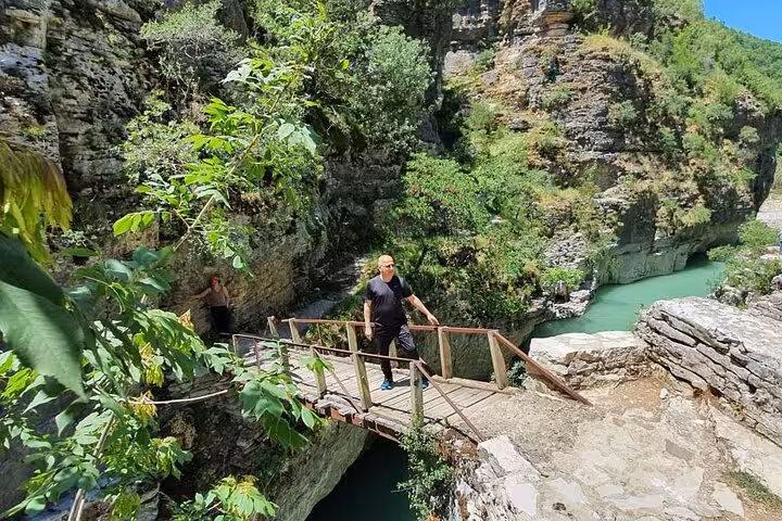 Tourist explores a rustic wooden bridge amidst the striking natural beauty of Osum Canyon's rocky landscape.