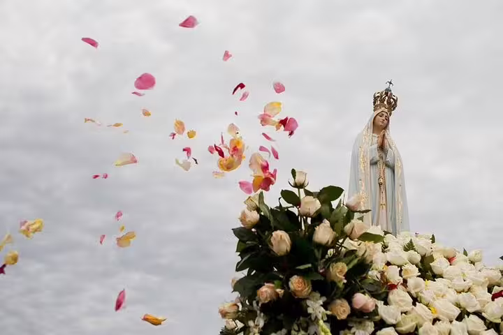 Statue of Our Lady of Fatima adorned with roses amidst petals in the air at the Fatima Shrine, Portugal.