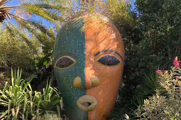 Giant mosaic mask sculpture in a lush garden stop on the Ourika Valley day trip from Marrakech, Morocco
