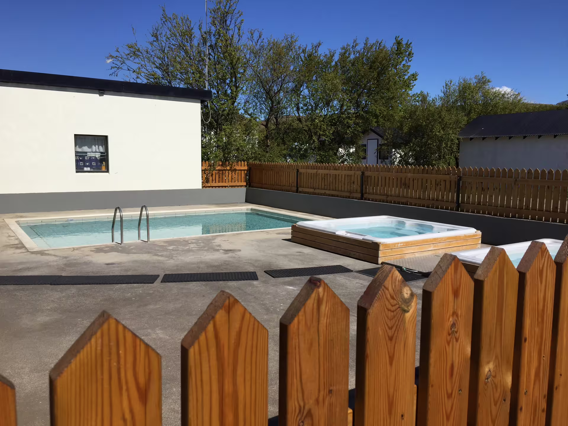 Fenced outdoor pool area with a hot tub and clear skies, offering relaxation after an extreme river rafting adventure.