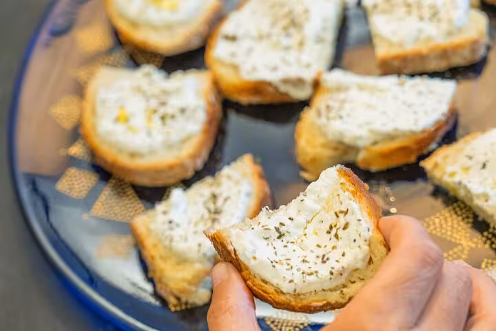 Close-up of hand holding a slice of bread with creamy spread, part of a seafood tasting tour in the Riviera.