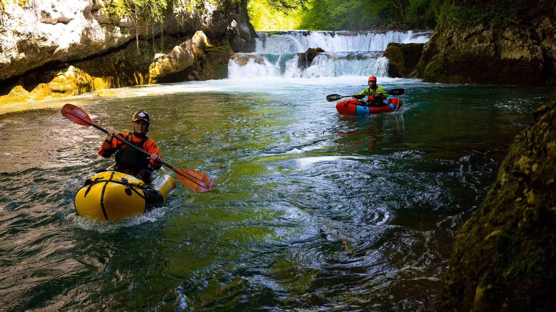 Adventurers packrafting through the scenic Mreznica River with cascading waterfalls and lush greenery.